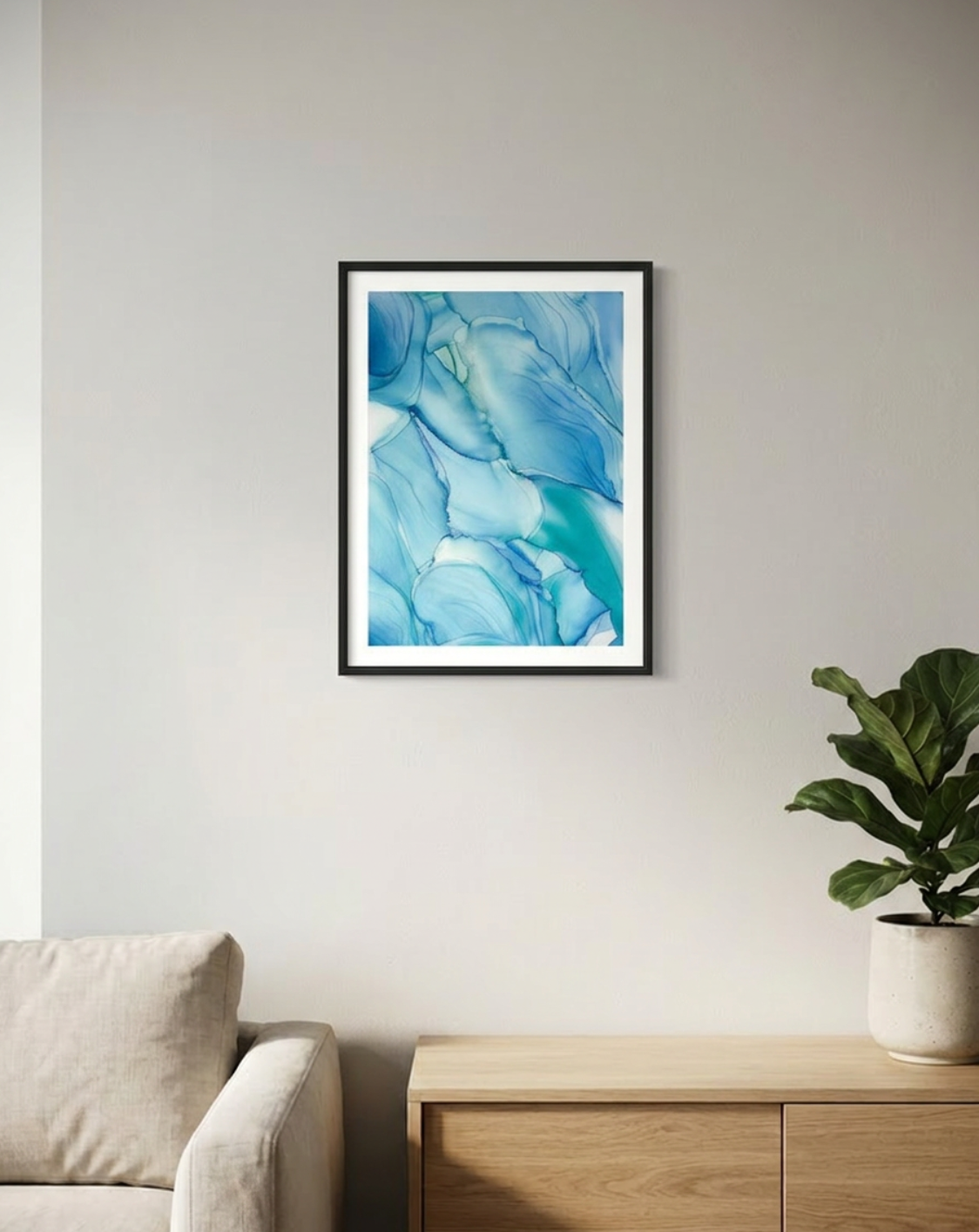 Framed abstract blue artwork on a wall above a beige sofa with a wooden side table and plant.